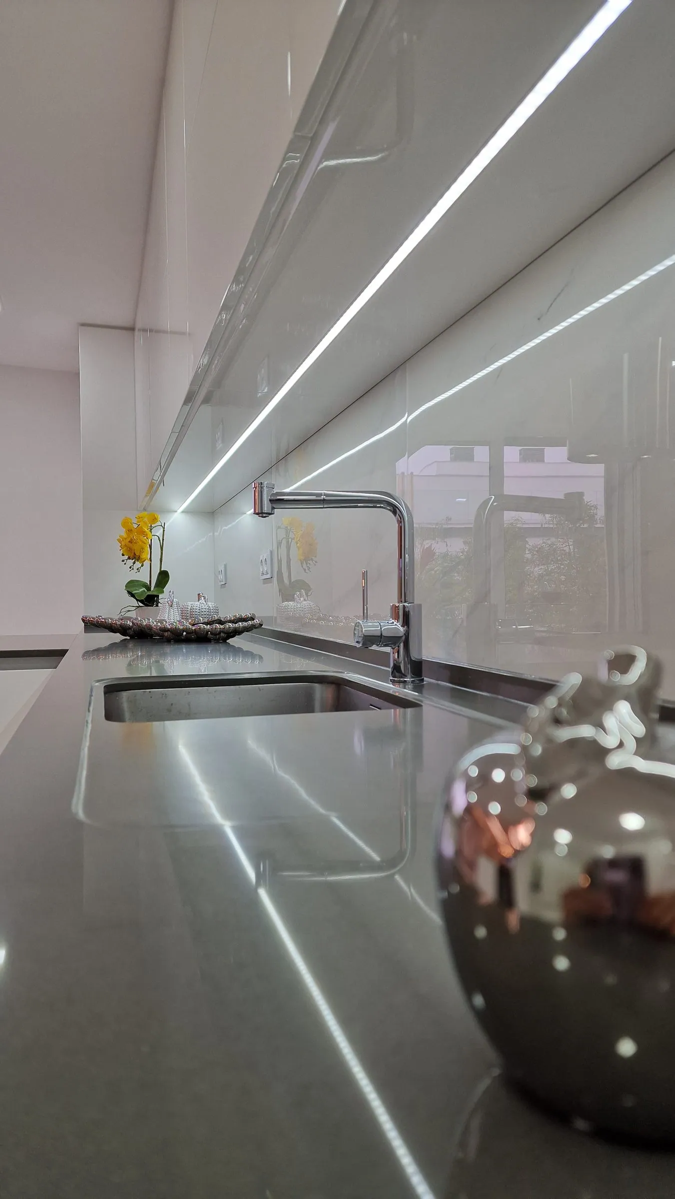 Cozinha com bancada cinzenta, torneira alta e luz linear no teto.