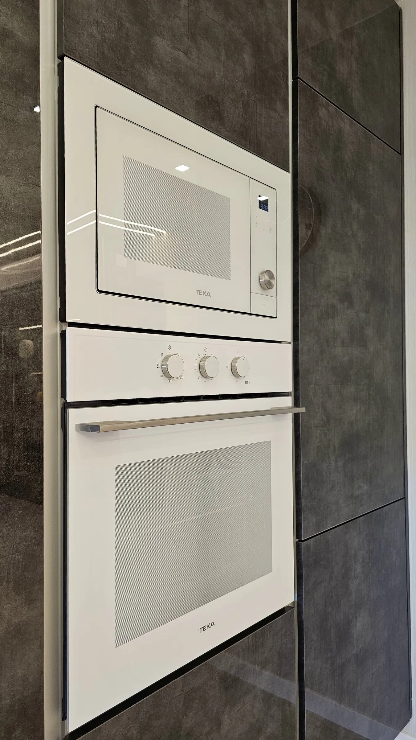 Forno e micro-ondas brancos encastrados na coluna escura.