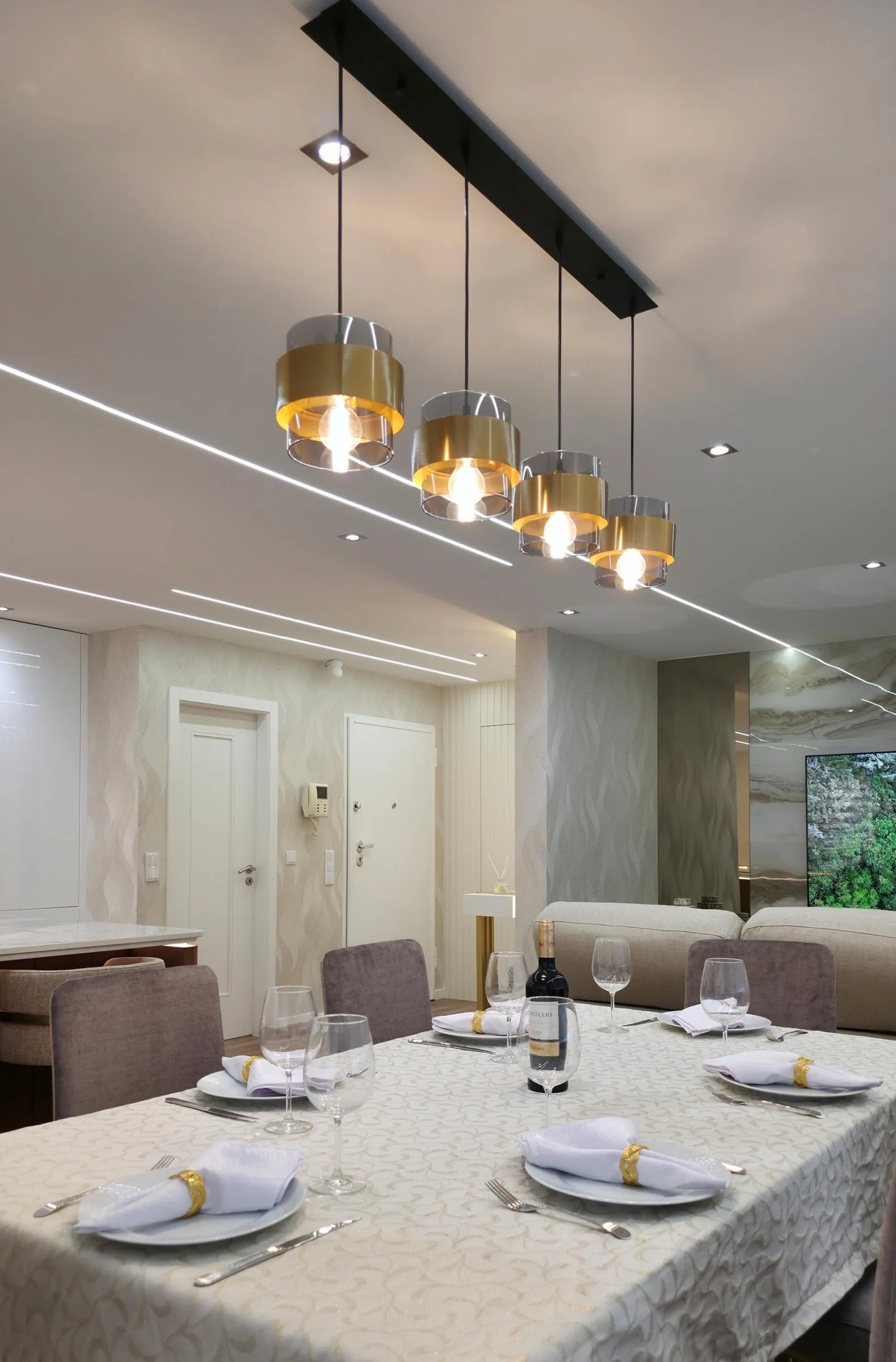 Mesa de jantar posta, com candeeiros dourados suspensos de uma calha preta.
