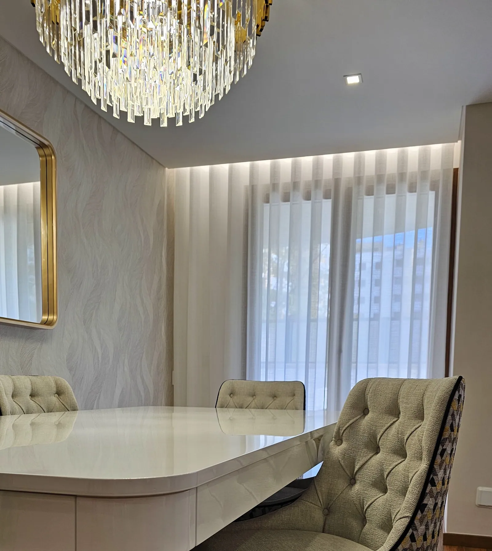 Cadeira capitonê junto à mesa de jantar e cortinados até ao chão.