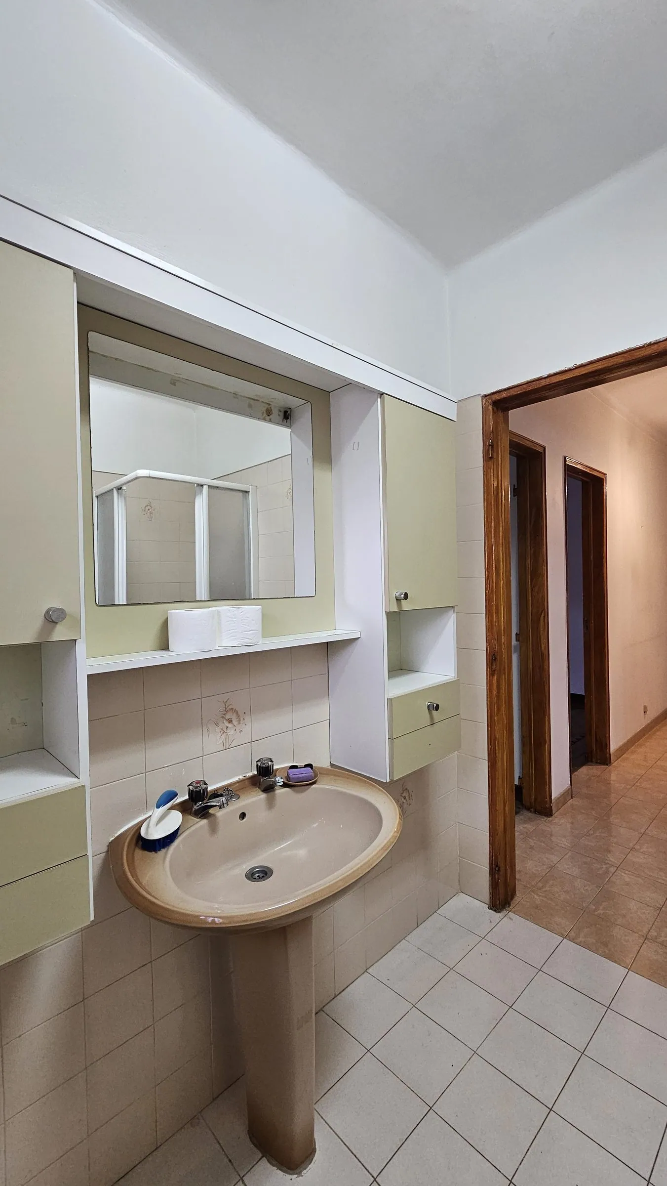 A casa de banho antes, com lavatório de pé e armário verde-claro.