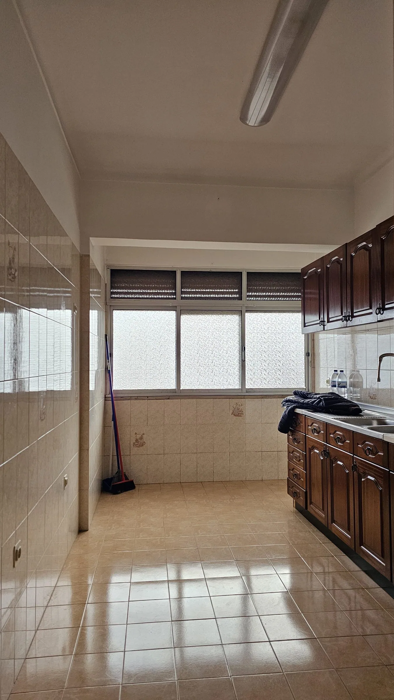 A cozinha antes, com armários de madeira escura e azulejos bege.