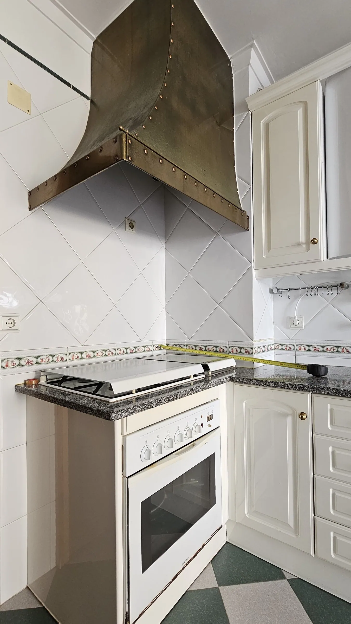 O fogão antigo, entre azulejo branco e armários creme.