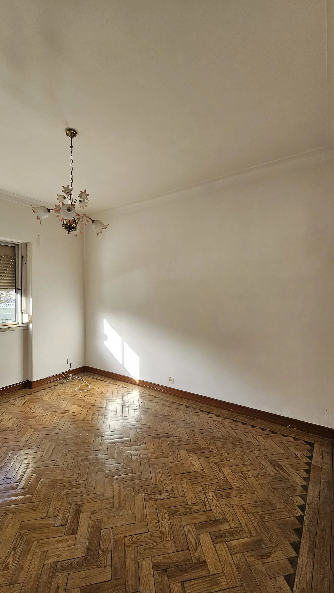 O quarto antes, vazio, com soalho em espinha e lustre.