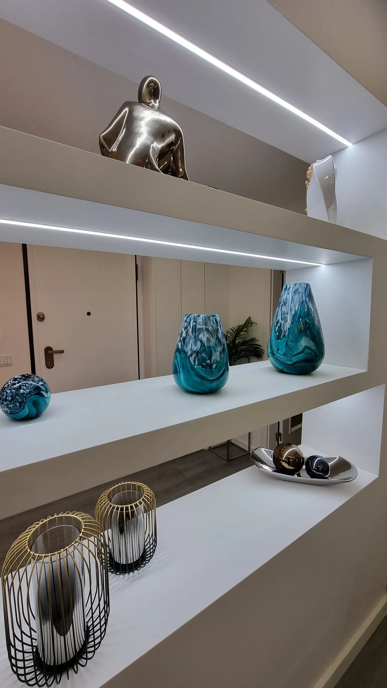 Prateleiras iluminadas com vasos de vidro azul e peças de metal.