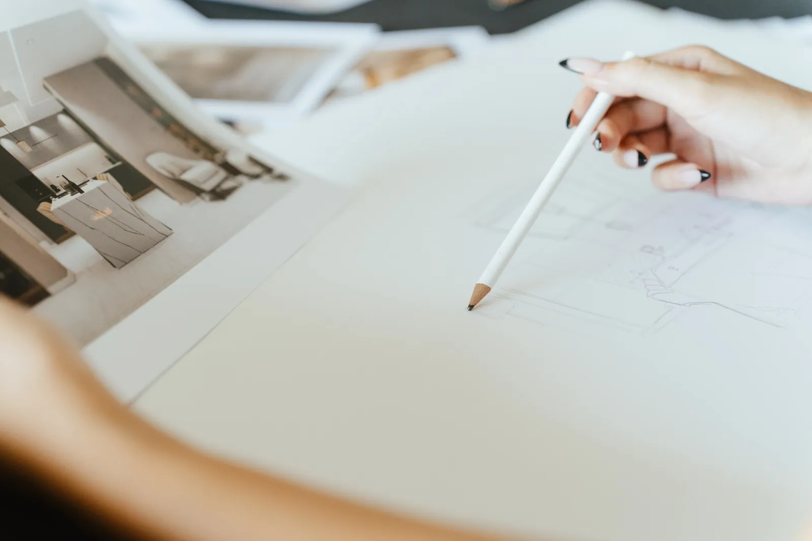 Um lápis a desenhar sobre papel branco, com renders impressos ao lado.